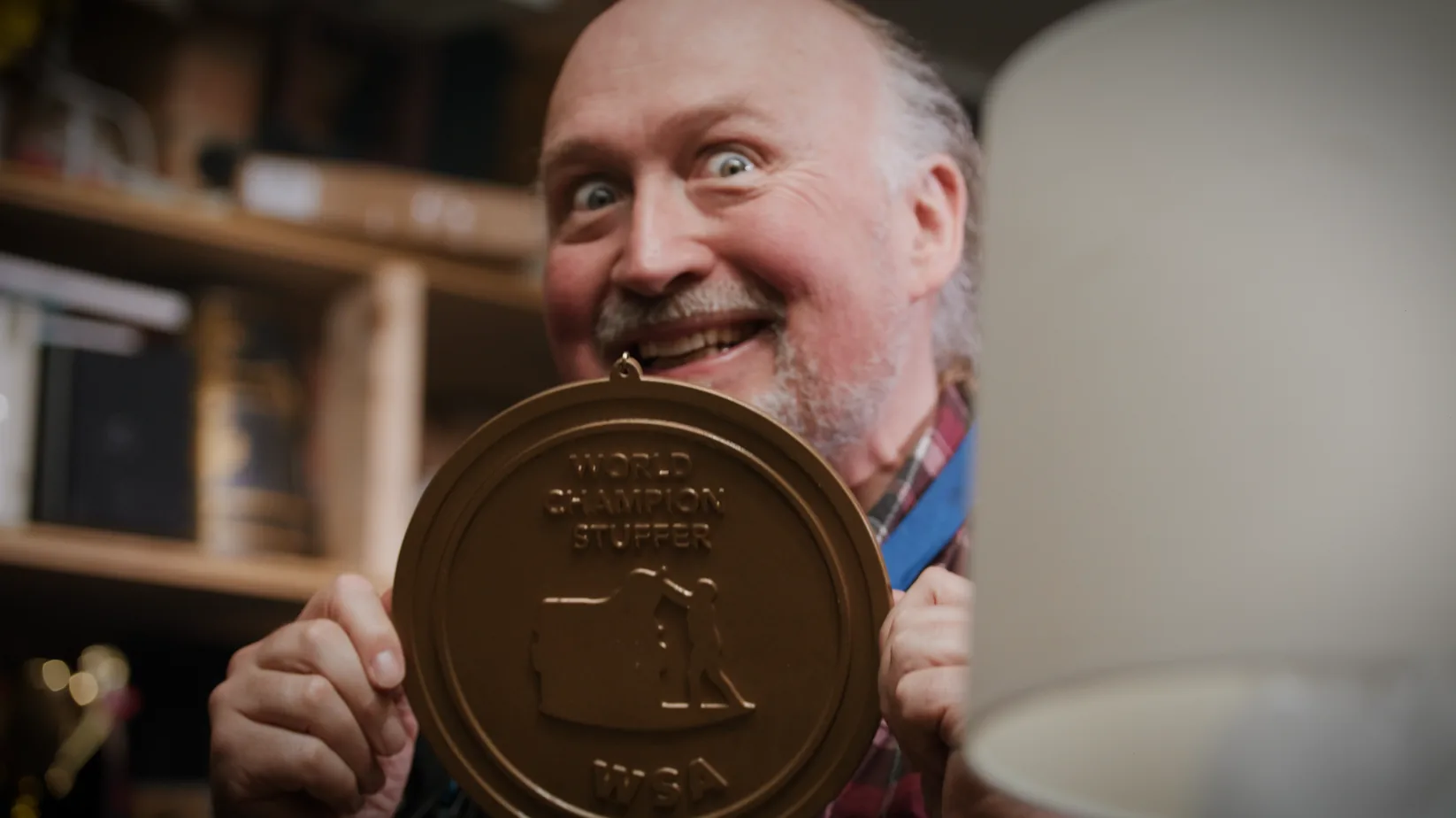 A grinning man holds up a “World Champion Stuffer” medal