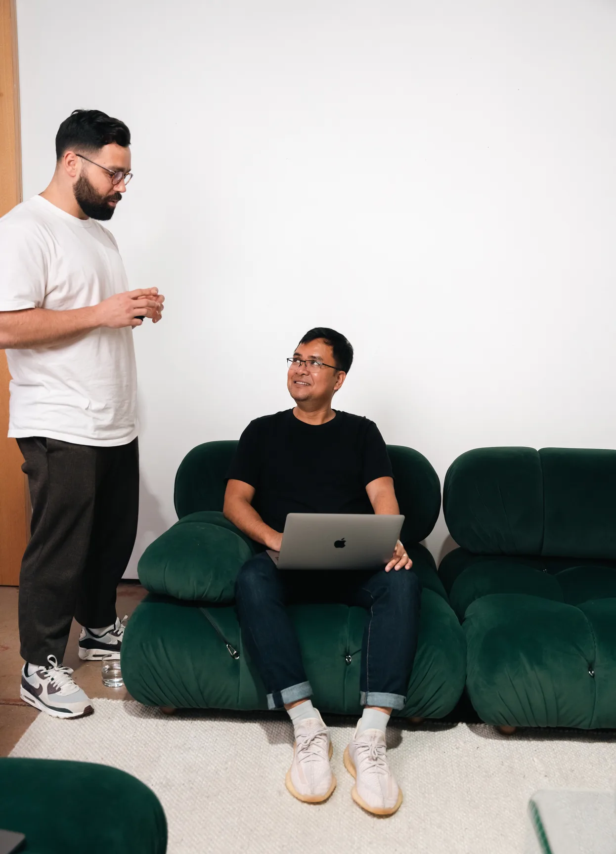 Two of the Media Exchange team talking on a green sofa, one with a laptop