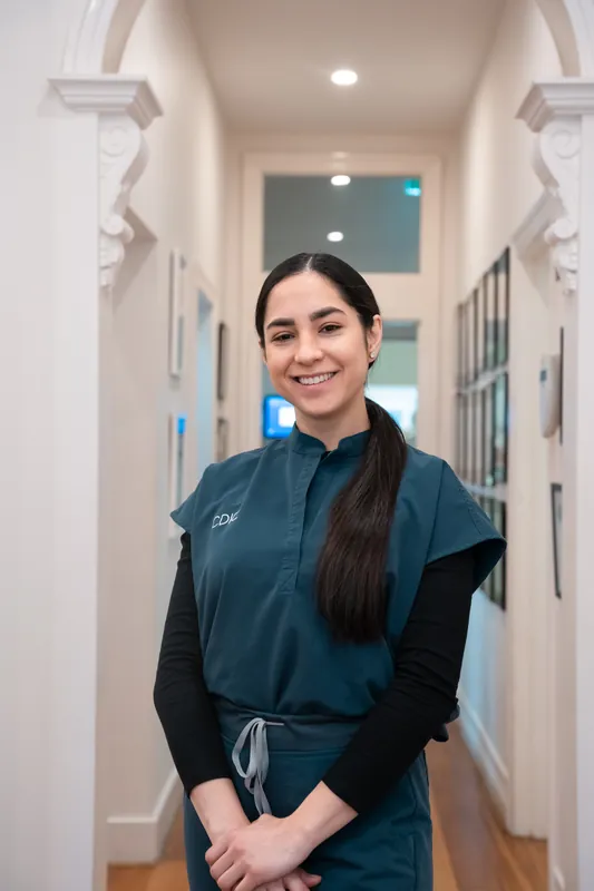 Smiling clinician in teal scrubs standing in a bright clinic hallway