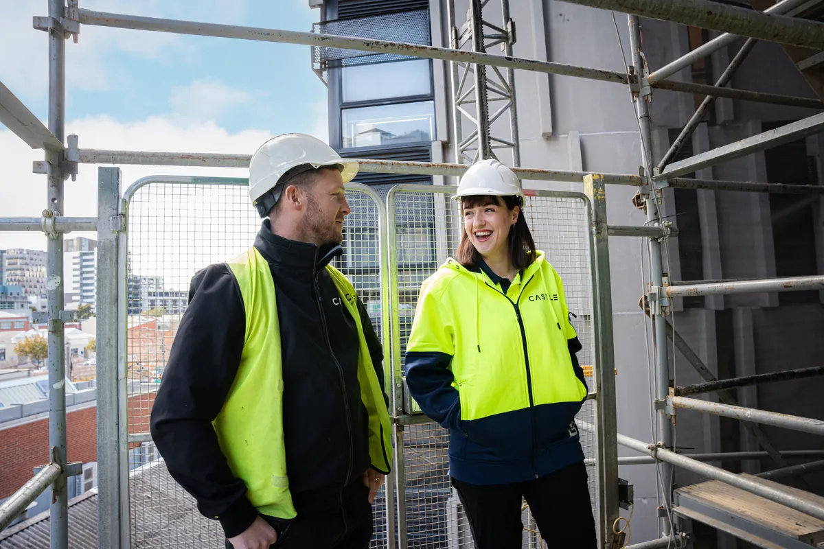 Two construction workers in hard hats and hi-vis chatting beside scaffolding on a building site