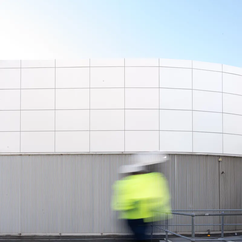 Worker in hi-vis walking past a curved white building facade, blurred in motion