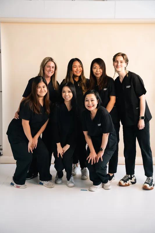 Dental team of nine in black scrubs posing together against a cream wall