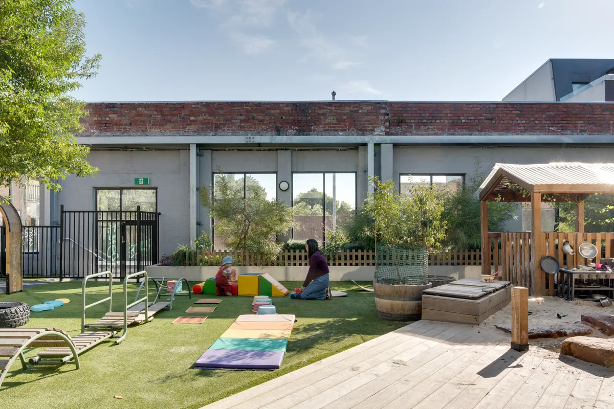 Outdoor play area of an early learning centre with artificial turf, timber decking and play equipment
