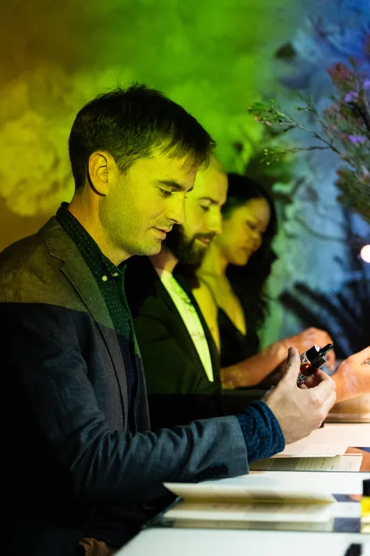 Guests seated at a table under green and yellow event lighting, the nearest in a dark jacket looking down