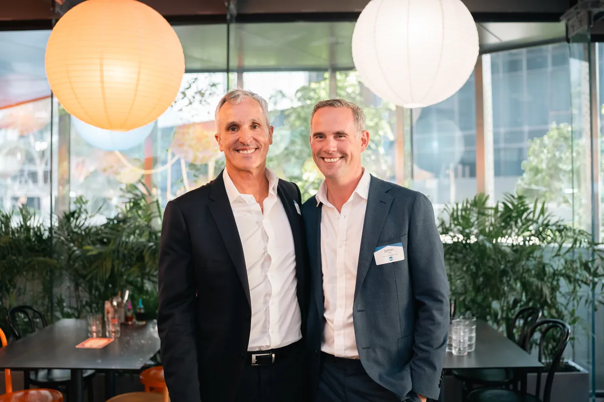 Two men in suits smiling side by side at an evening function under paper lanterns