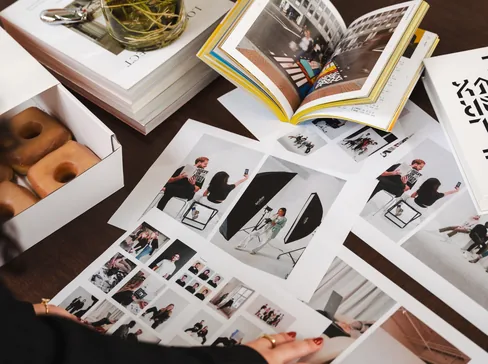 Printed brand collateral and photo layouts spread across a table beside open books