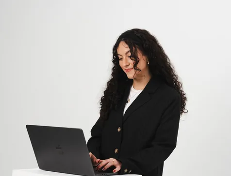 A designer in a black blazer working on a laptop in a white studio