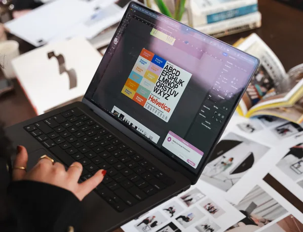 Hands on a laptop showing a website design layout, surrounded by printed page mock-ups