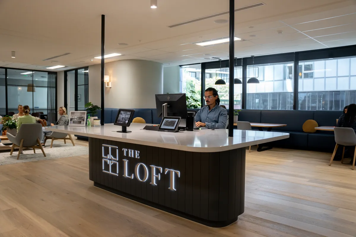 Reception desk branded The Loft in a bright office, with a lounge and meeting areas behind