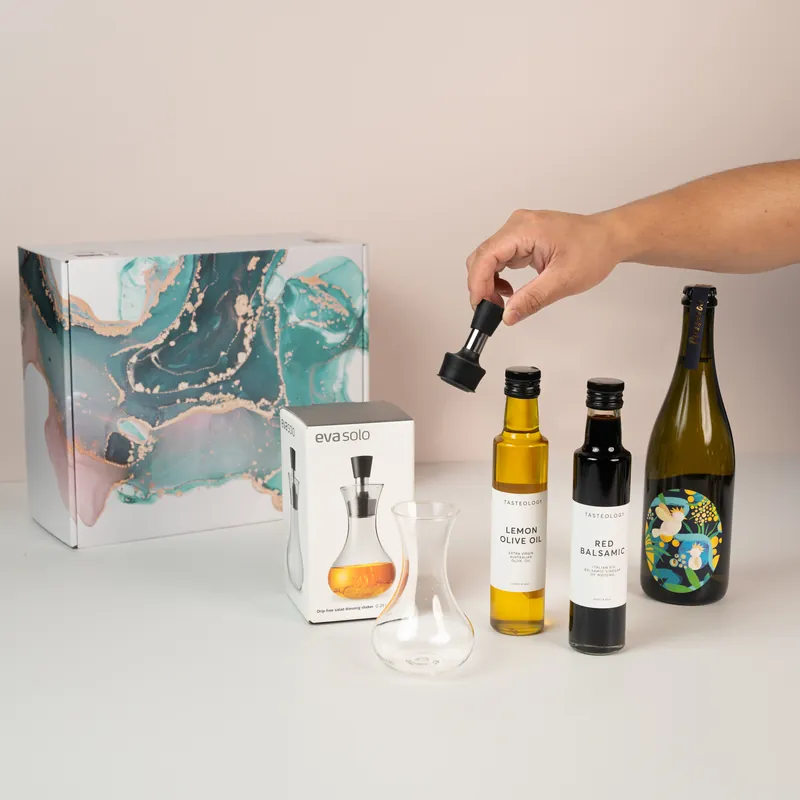 Hand fitting a pourer to a bottle among olive oils, vinegar and wine beside a marbled gift box