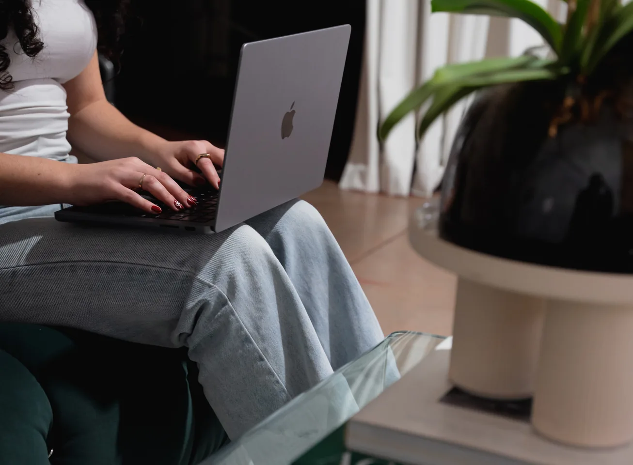 Woman typing on a laptop beside a potted plant