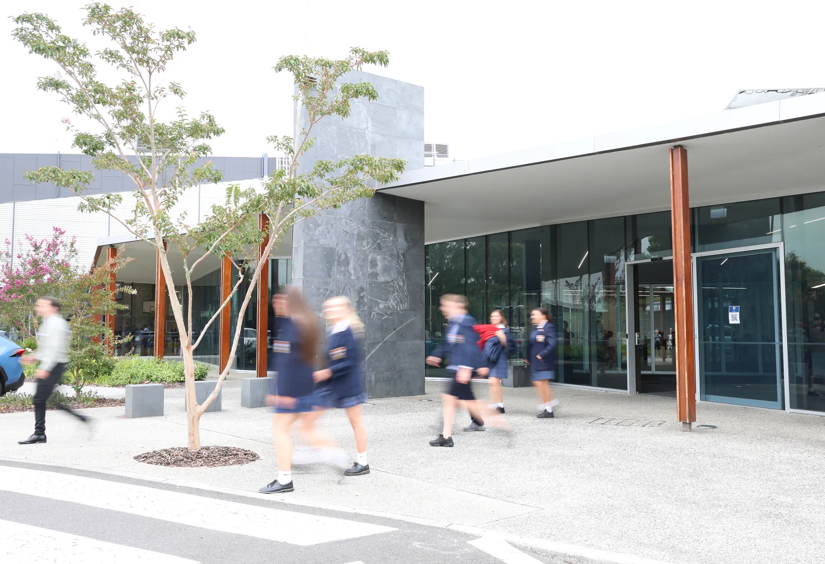 Students in St Francis Xavier College uniforms walking past the stone-and-glass entrance of a campus building
