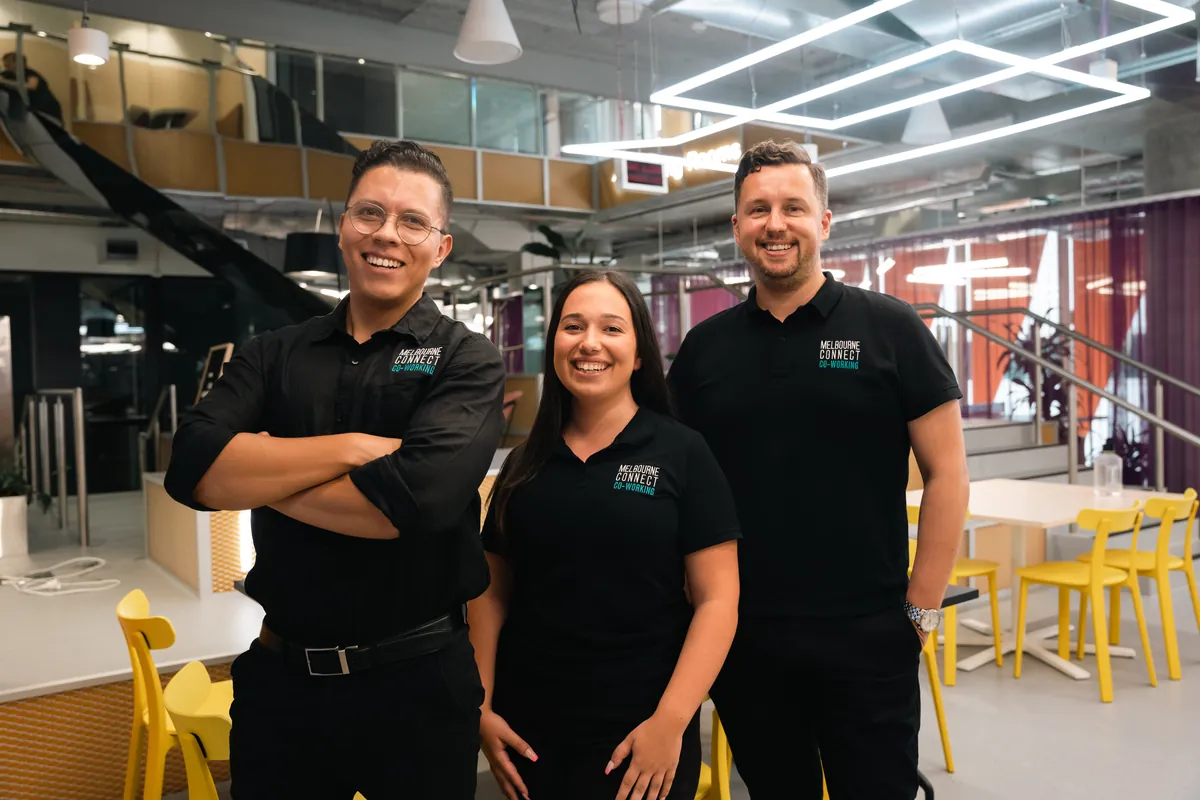 Three team members in branded black polos standing together in a modern open-plan workspace
