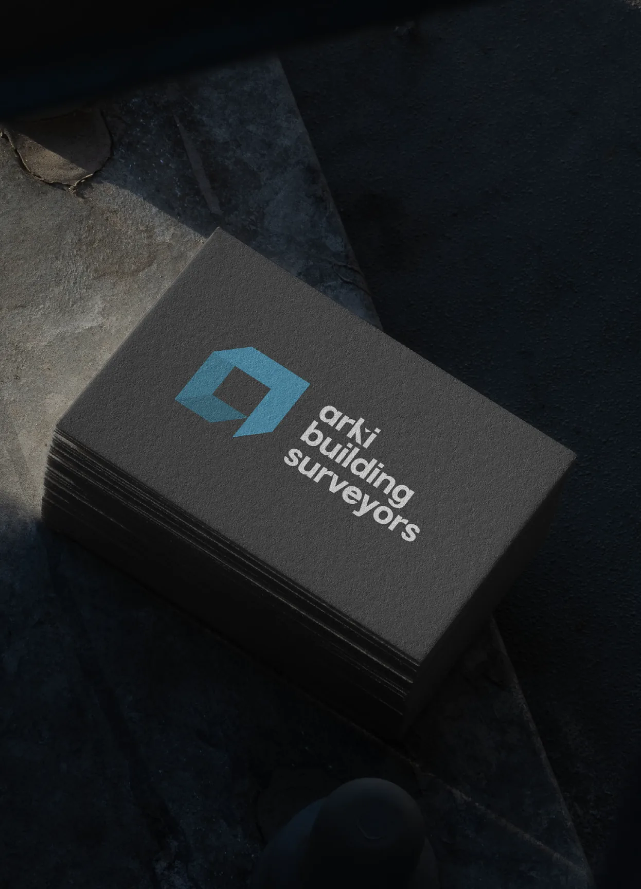 Stack of dark business cards printed with the arki building surveyors logo
