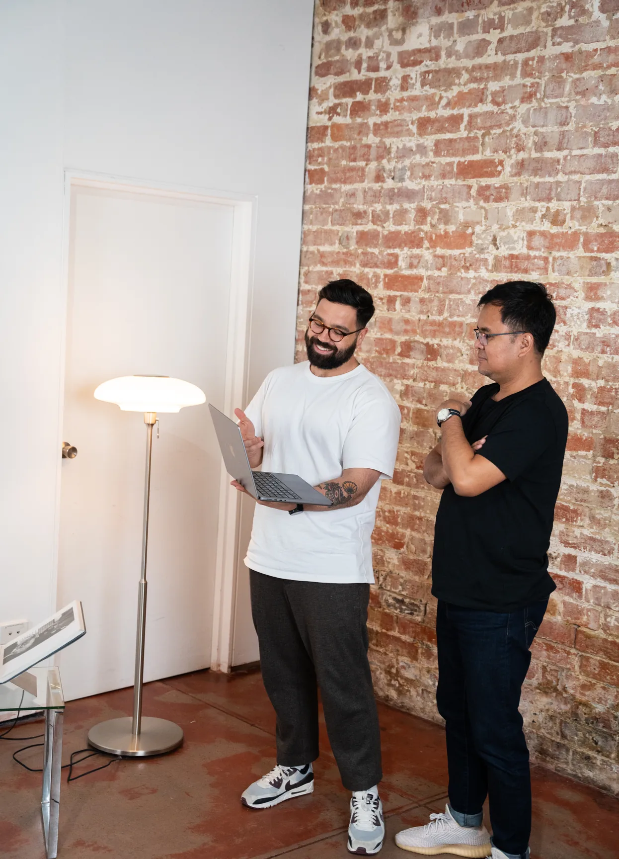 Two Media Exchange team members reviewing work on a laptop against a brick wall