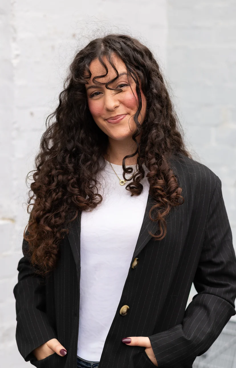 Portrait of Emily Cabral, smiling in a black blazer against a white brick wall