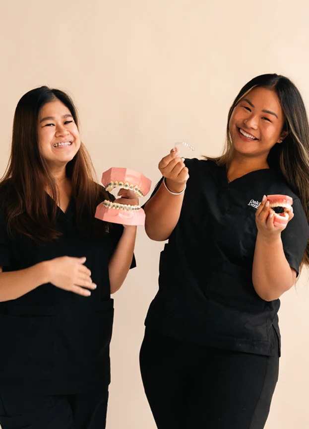 Two Oakleigh Dental team members in black scrubs laughing as they hold up dental models