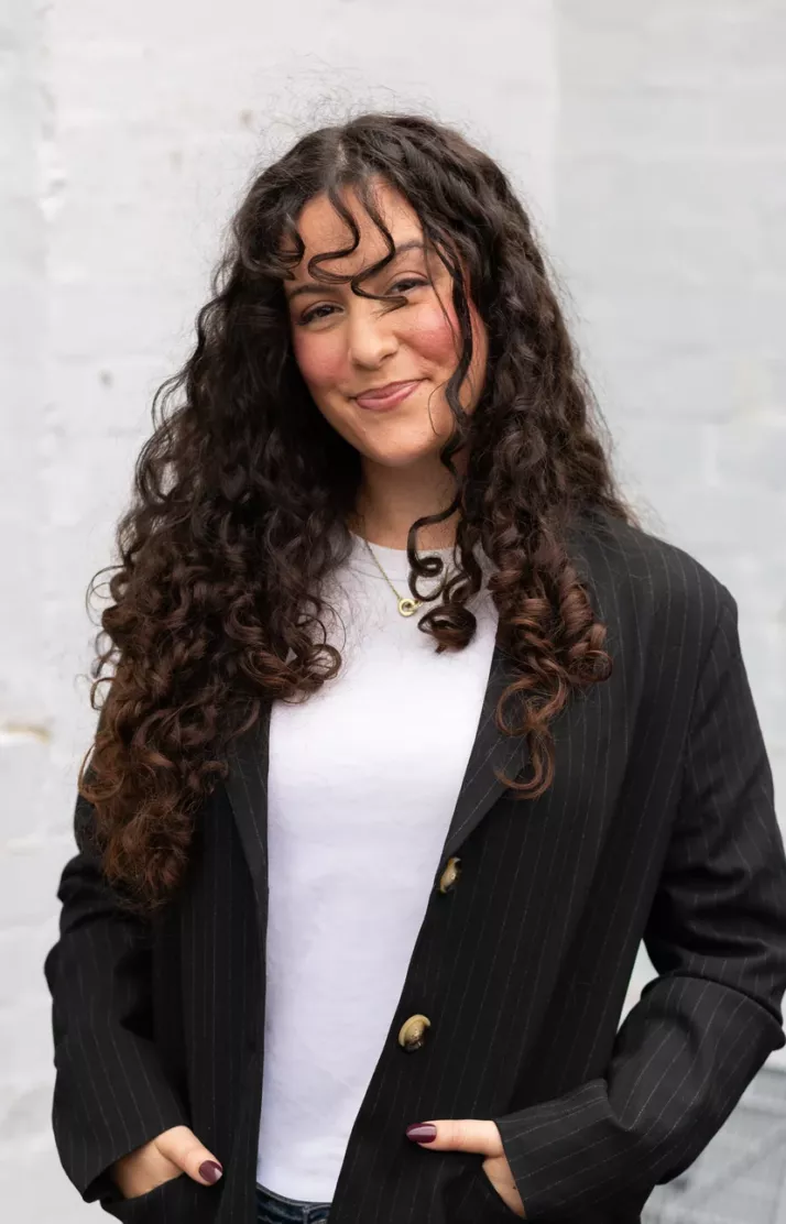 Portrait of Emily Cabral, smiling in a black blazer against a white brick wall